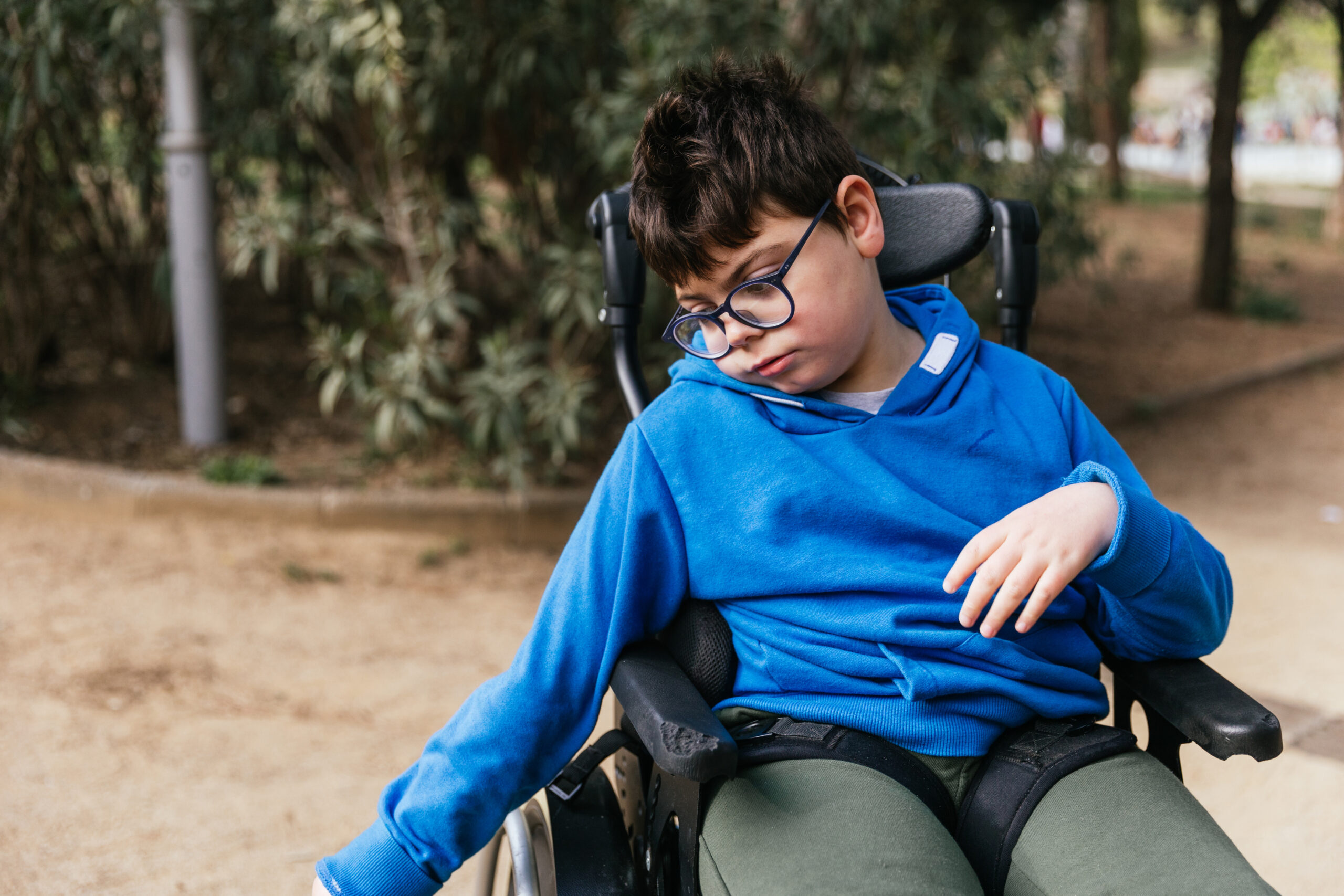 Child with multiple disabilities in a wheelchair enjoying the day outdoors in the park.