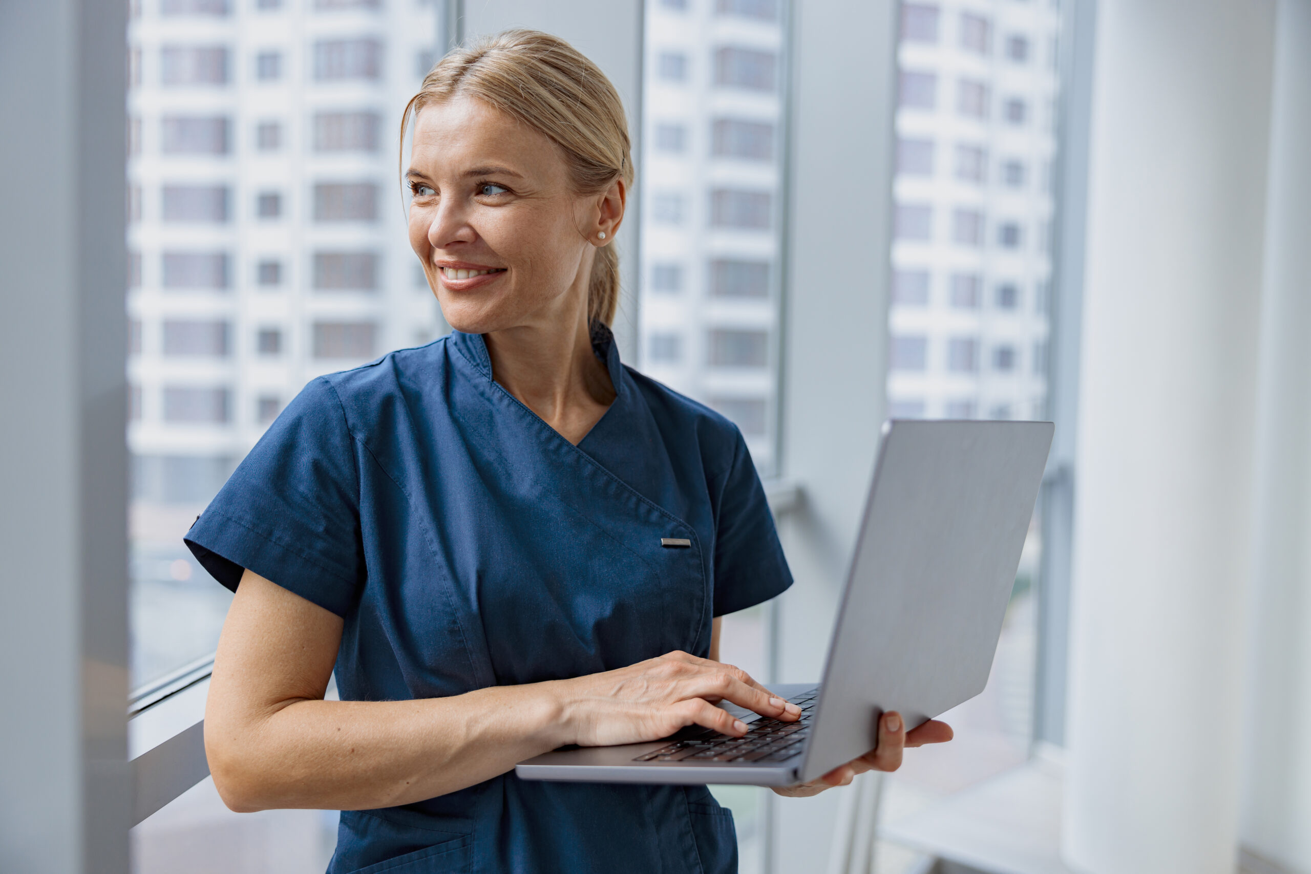 Female healthcare worker using laptop while working at doctor's office and looking window