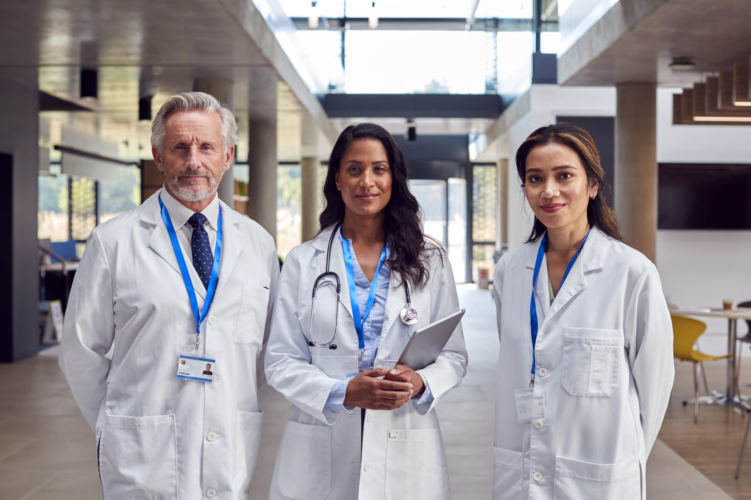 Portrait Of Medical Staff Wearing White Coats With Digital Tablet Having Meeting In Hospital