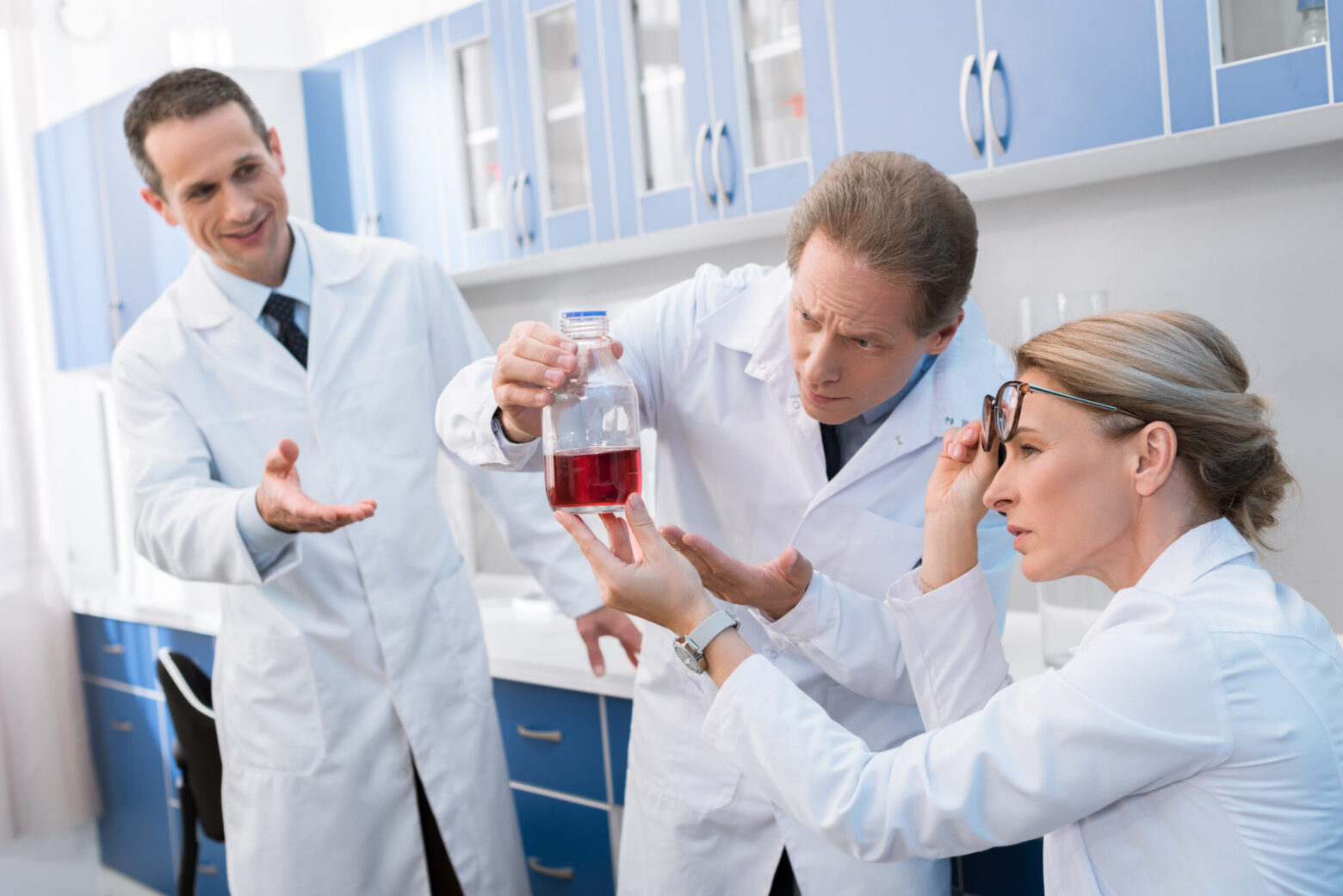 Team of professional scientists, examining a flask with bright red liquid in chemical laboratory