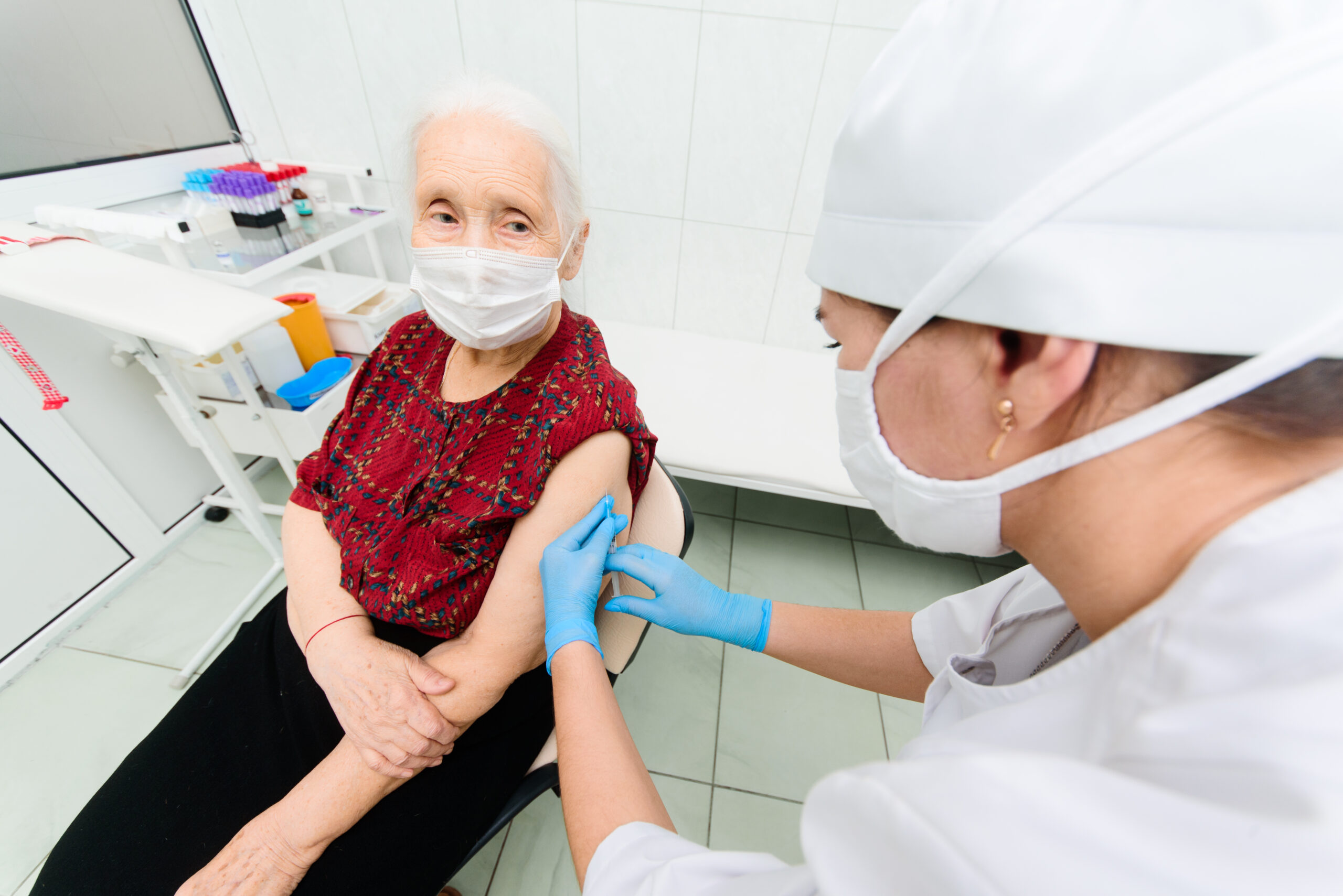nurse wearing a medical mask and rubber gloves is injecting or injecting a vaccine against the virus into the shoulder of an elderly woman