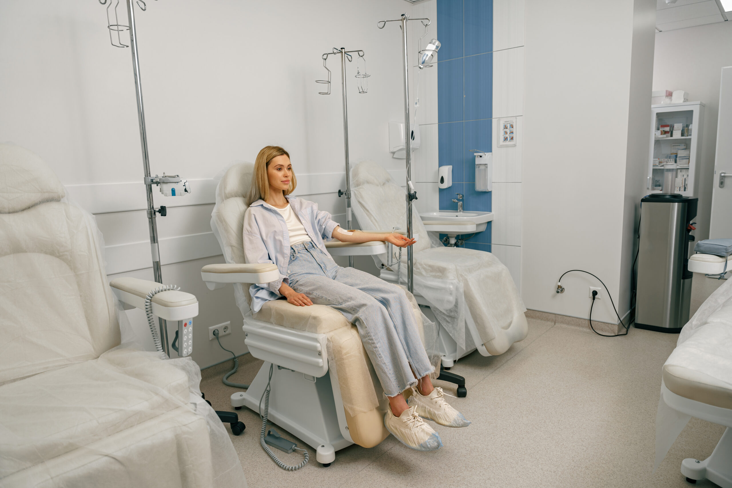 Pretty woman patient sitting in armchair while receiving IV infusion during treatment in hospital