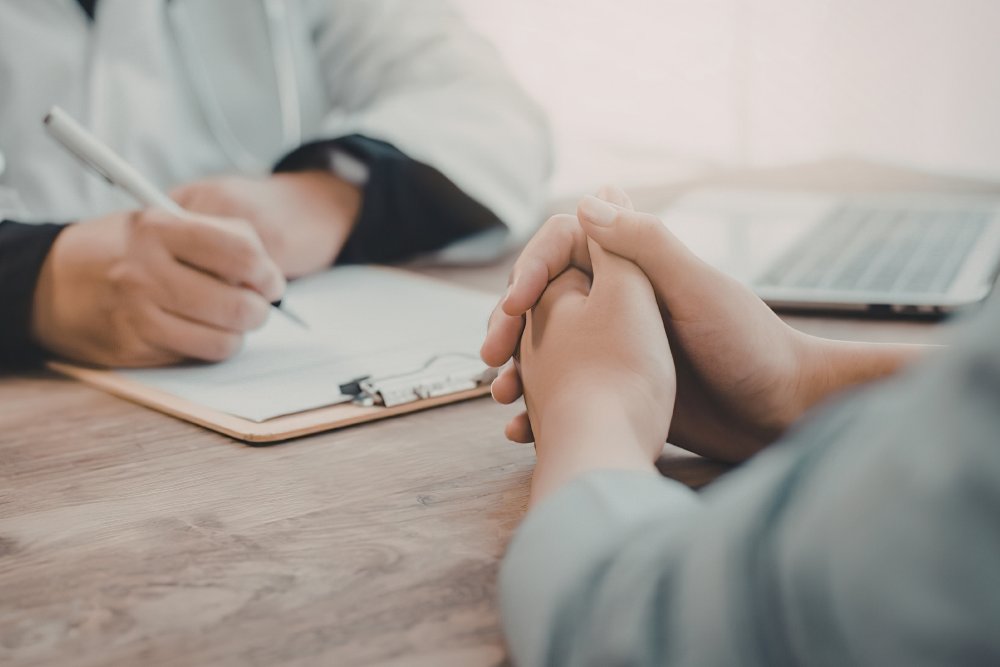 Aplicación para el cribado de salud en migrantes Médico tomando notas mientras un paciente sostiene sus manos.