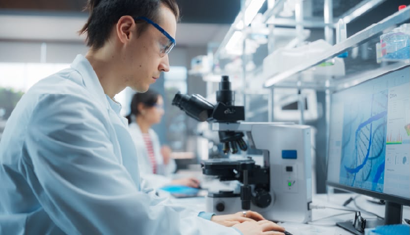 Científico trabajando en un laboratorio con microscopio y computadora