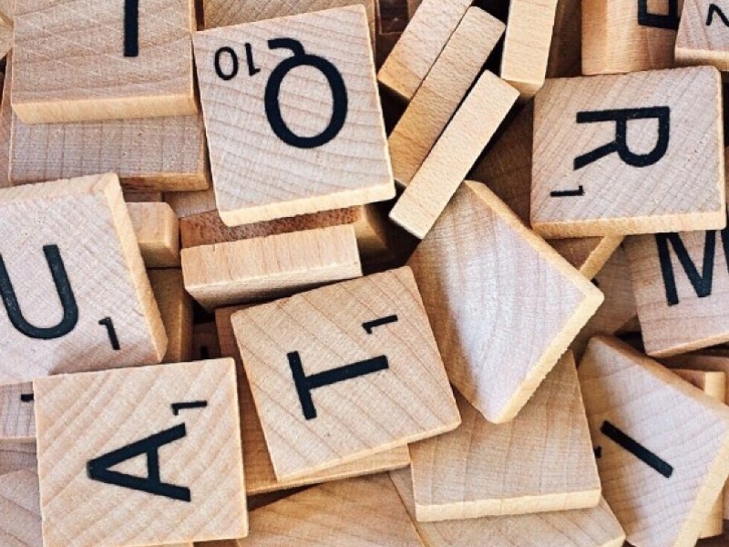 Letras de Scrabble y formación lingüística Fichas de letras de Scrabble sobre una superficie de madera