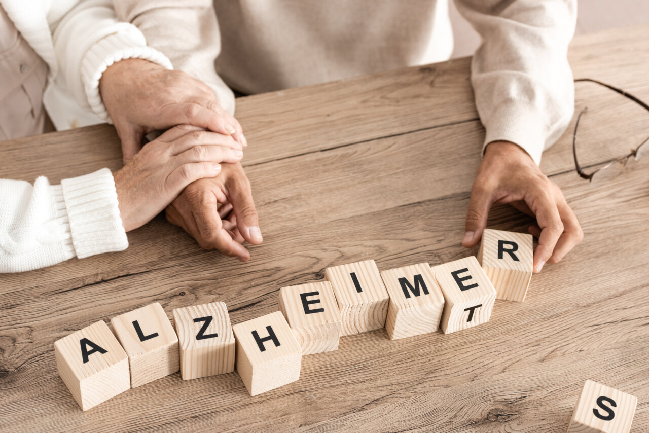 Manos de una pareja sosteniéndose mientras construyen la palabra Alzheimer con bloques.