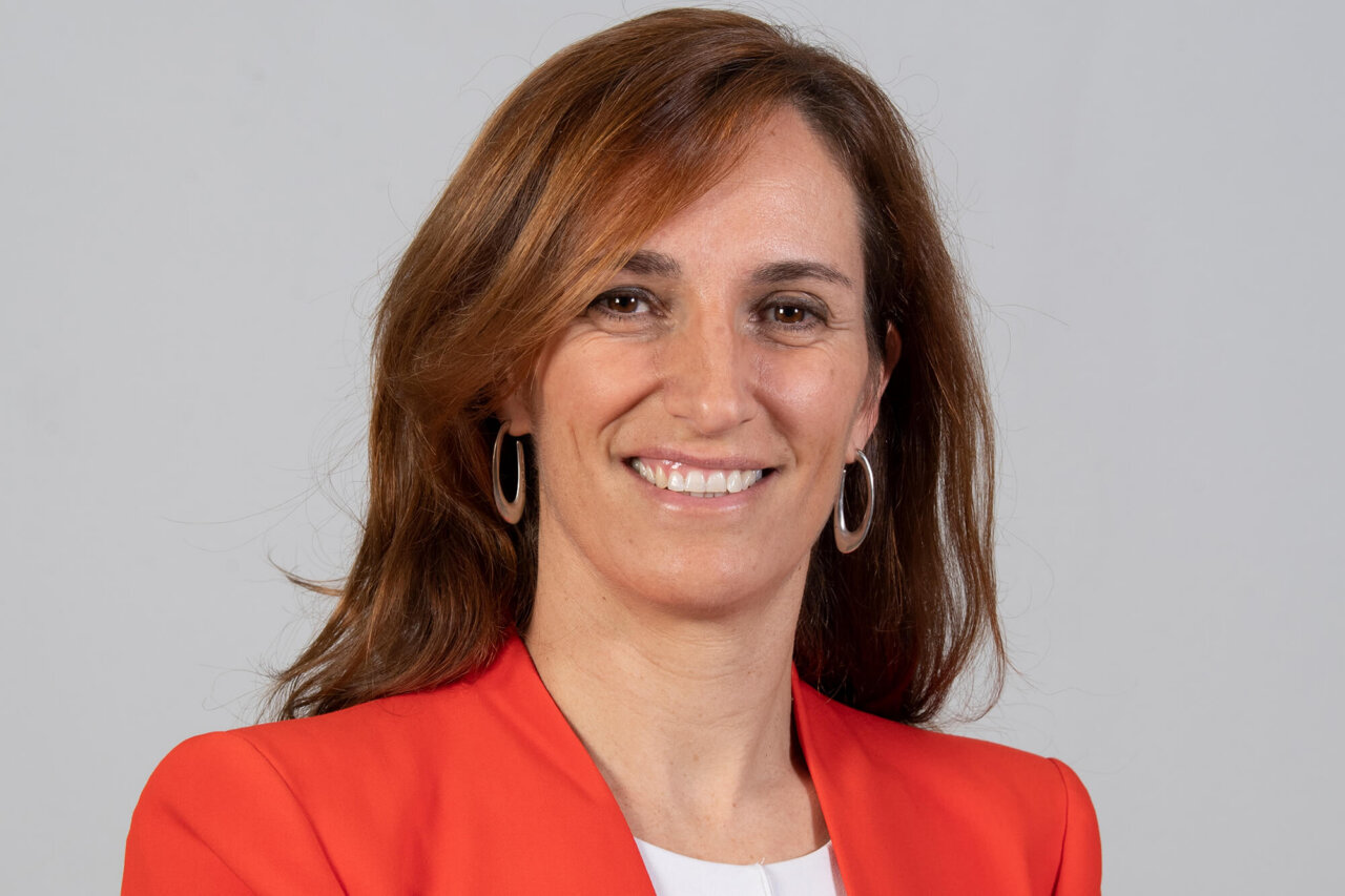Retrato de Mónica García, ministra de Sanidad, sonriendo con chaqueta roja.