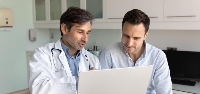 Médico y paciente revisando información sobre farmacovigilancia en una computadora portátil